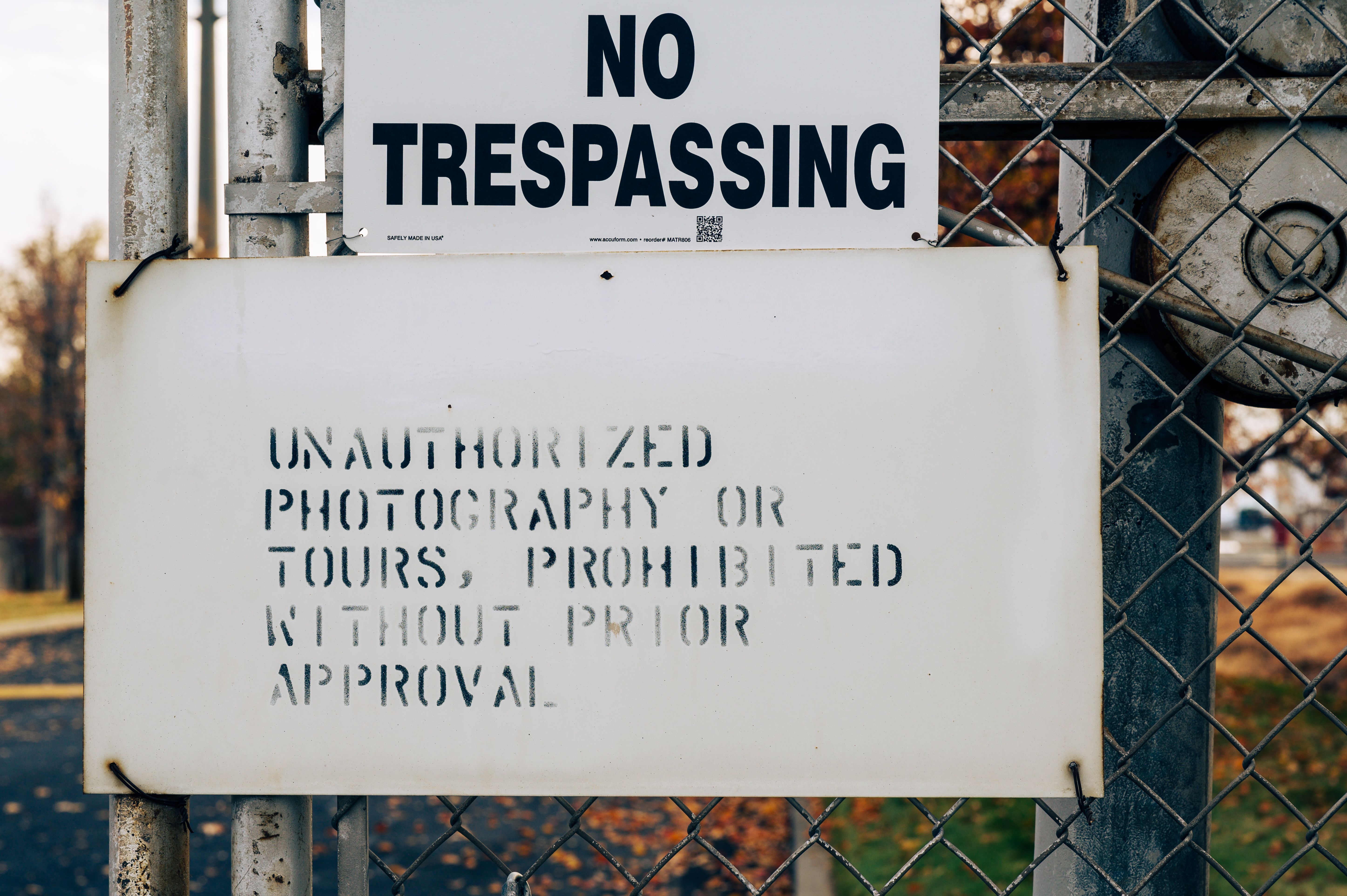 A warning sign on a metal fence prohibiting trespassing and unauthorized activities.