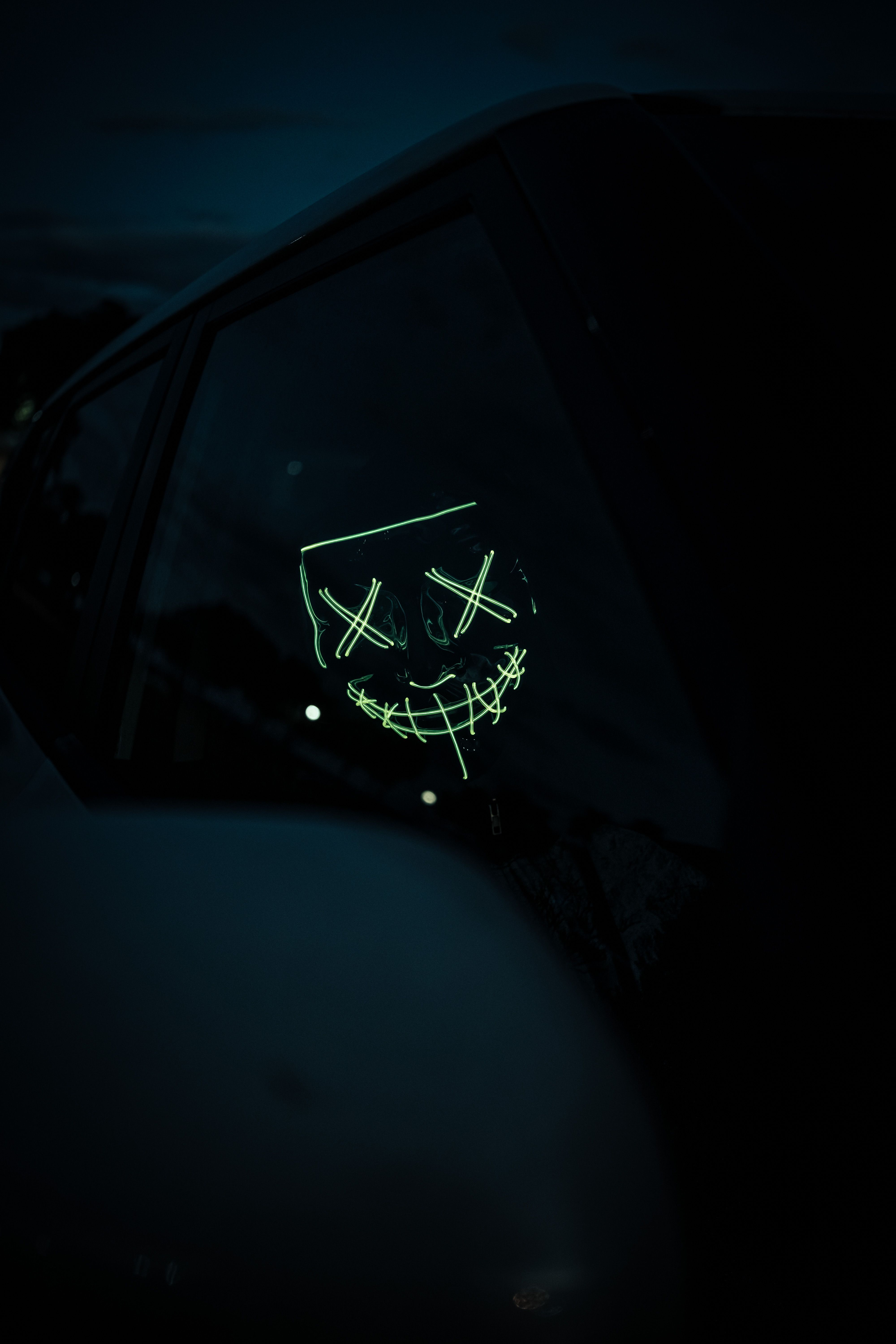 Eerie glow mask reflection on a car window, captured in a dark setting at night.