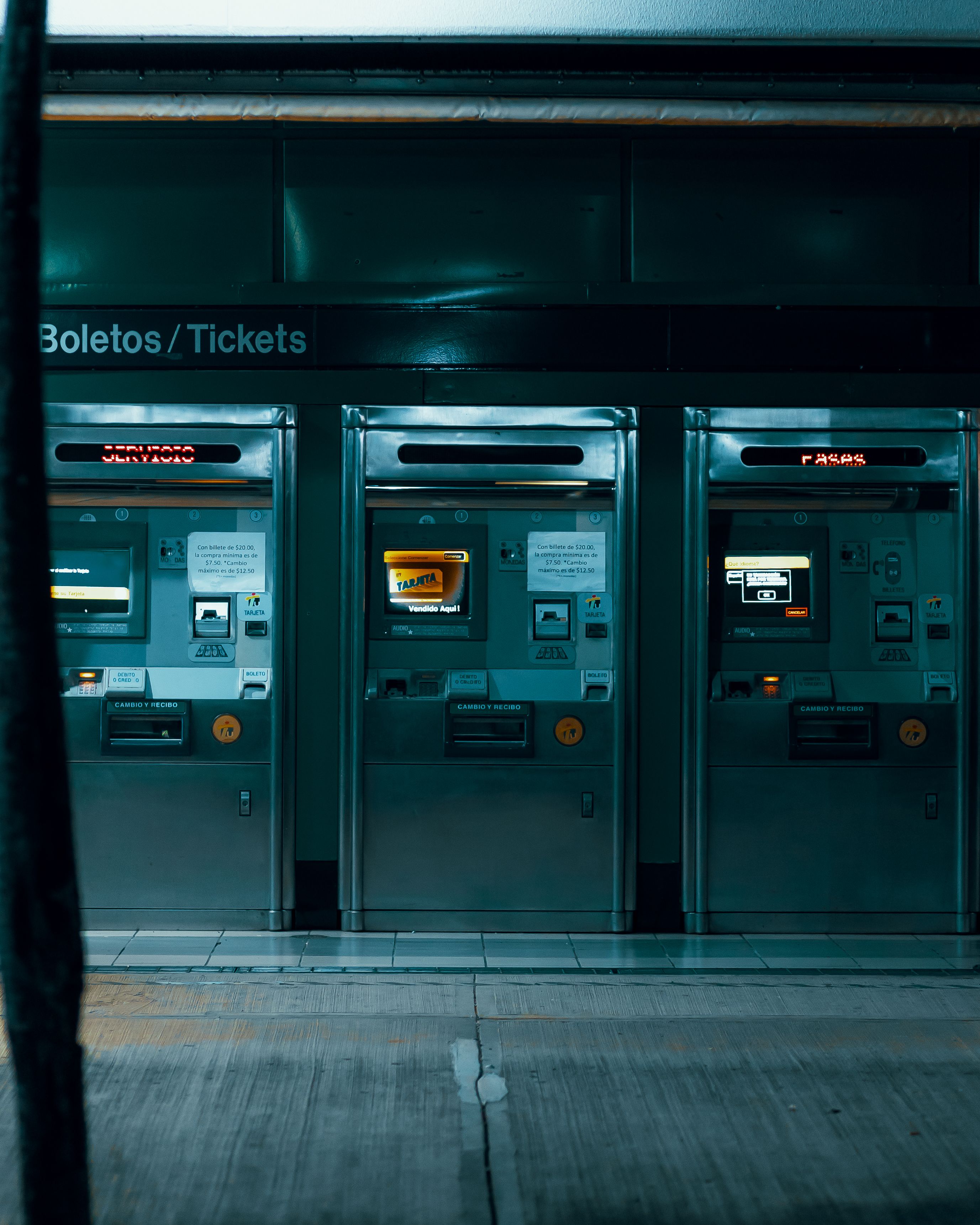 Three ticket vending machines in a dimly lit subway station, emphasizing modern urban technology.