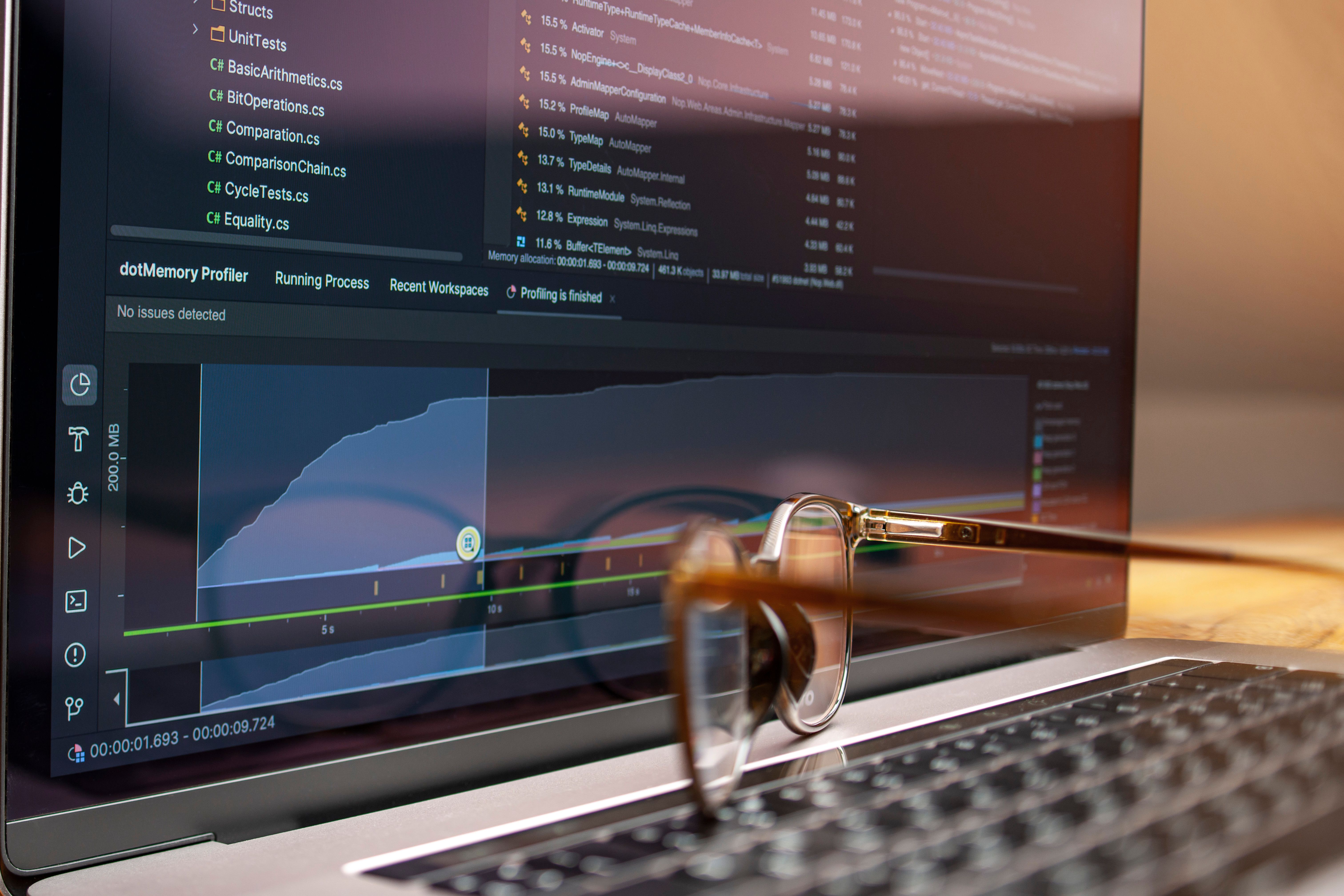 Laptop screen displaying code and performance graphs with eyeglasses resting on the keyboard.