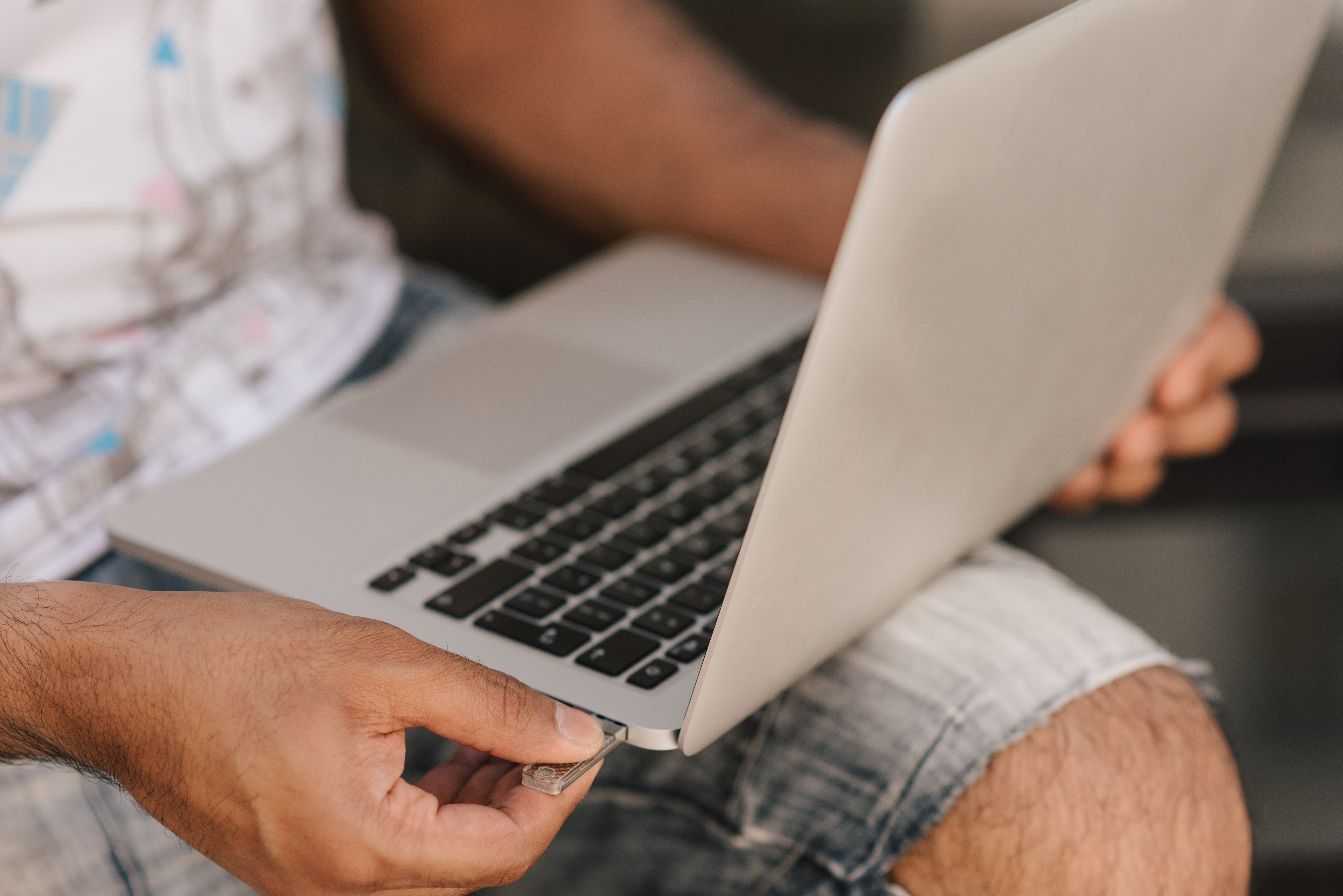 Crop unrecognizable male in casual shorts working on modern netbook placed on laps and inserting memory card in slot
