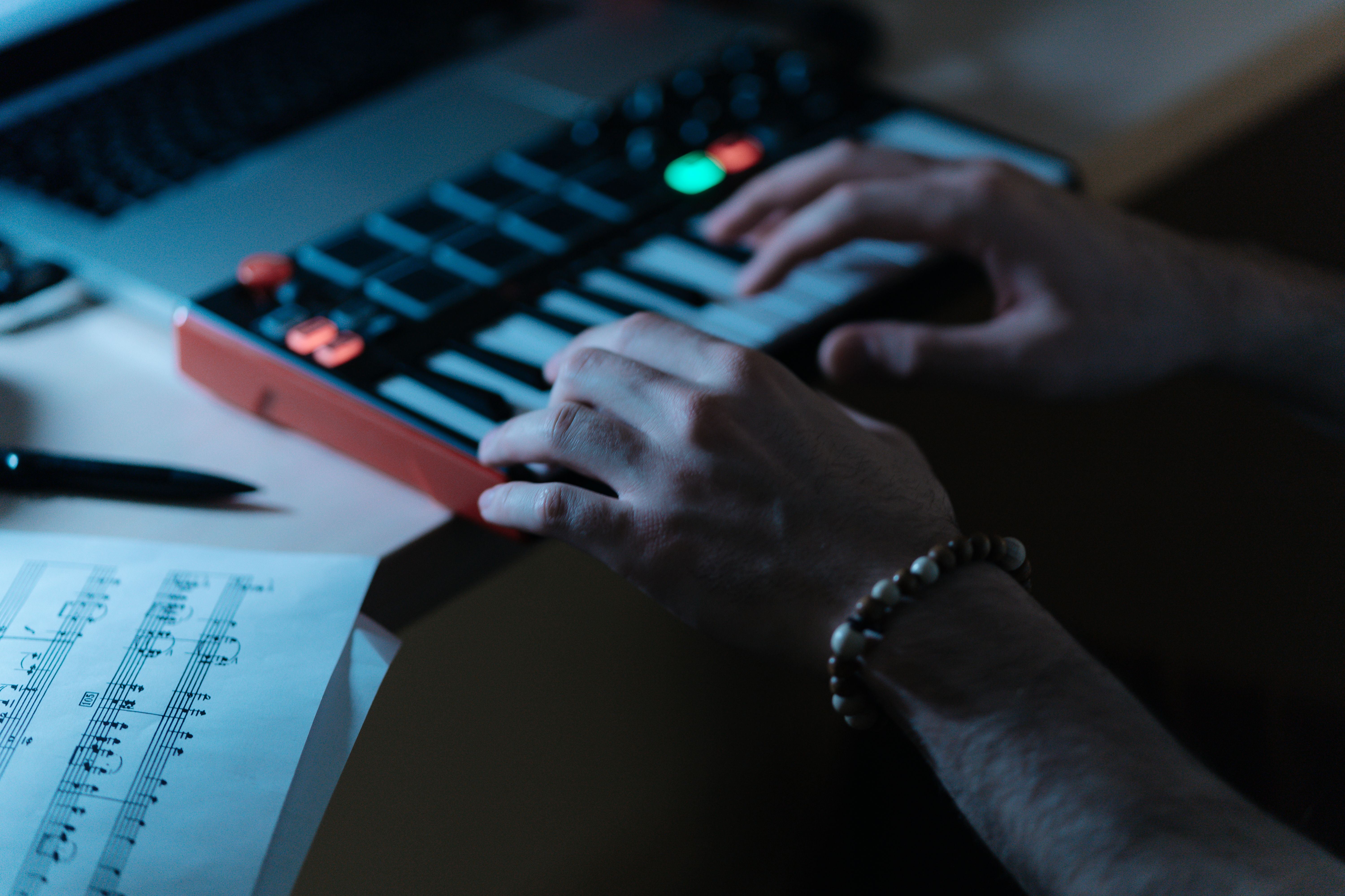 Close-up of hands playing a digital MIDI keyboard with sheet music nearby, indoors.